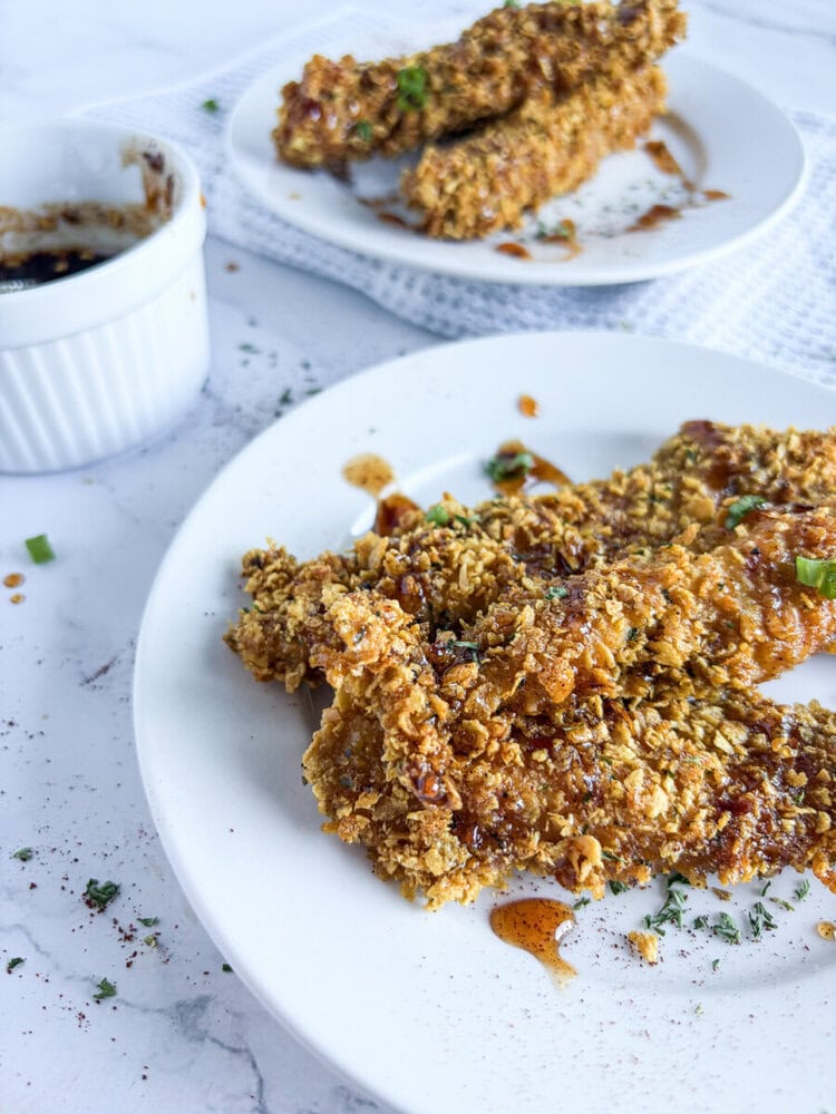 Crunchy baked chicken tenders with chili infused honey dipping sauce on white plates