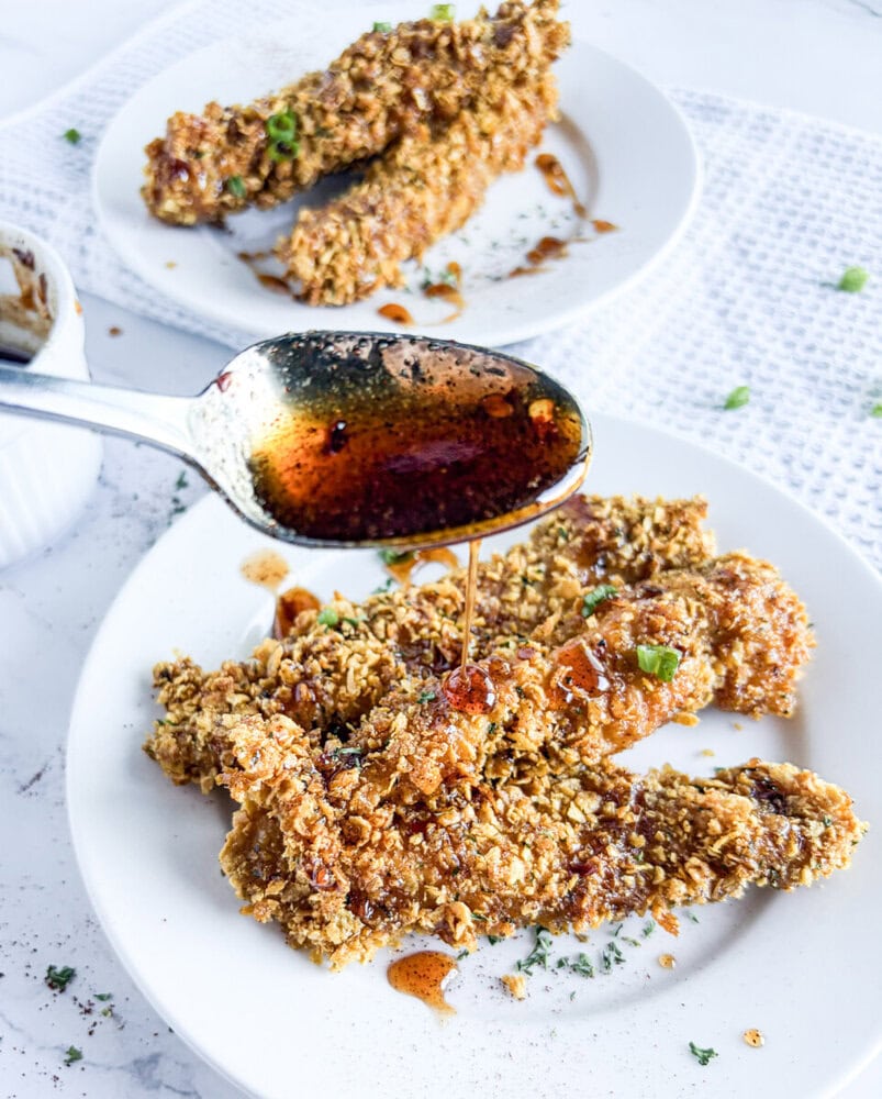 Crunchy baked chicken tenders with chili infused honey drizzle on white plate with herb garnish