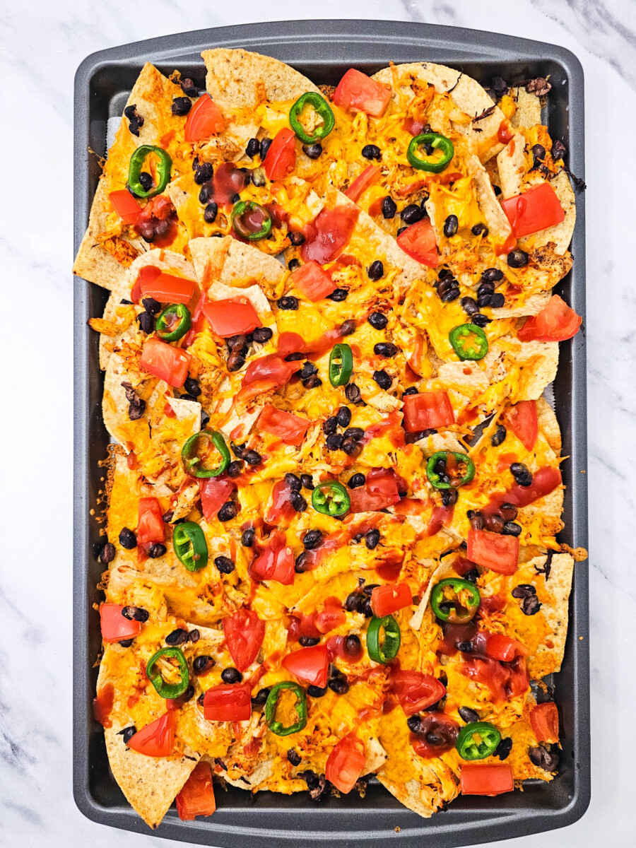 Sheet pan chicken nachos with cheese, black beans, red peppers, and jalape&ntilde;os on a baking sheet