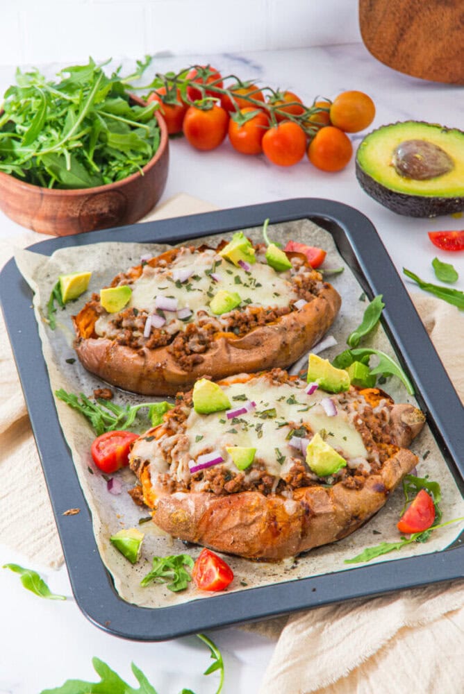Stuffed sweet potatoes with ground meat, melted cheese, and fresh toppings on a serving platter