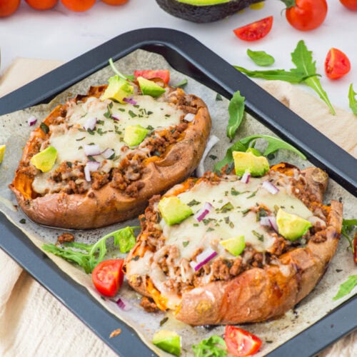 Stuffed sweet potatoes with ground meat, melted cheese, avocado and cilantro garnish on dark platter