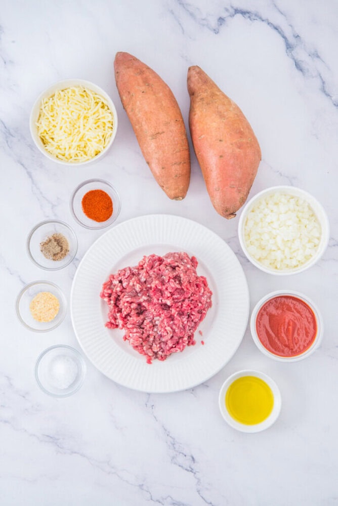 Stuffed sweet potato ingredients arranged on marble surface - sweet potatoes, ground beef, cheese, onions, and seasonings