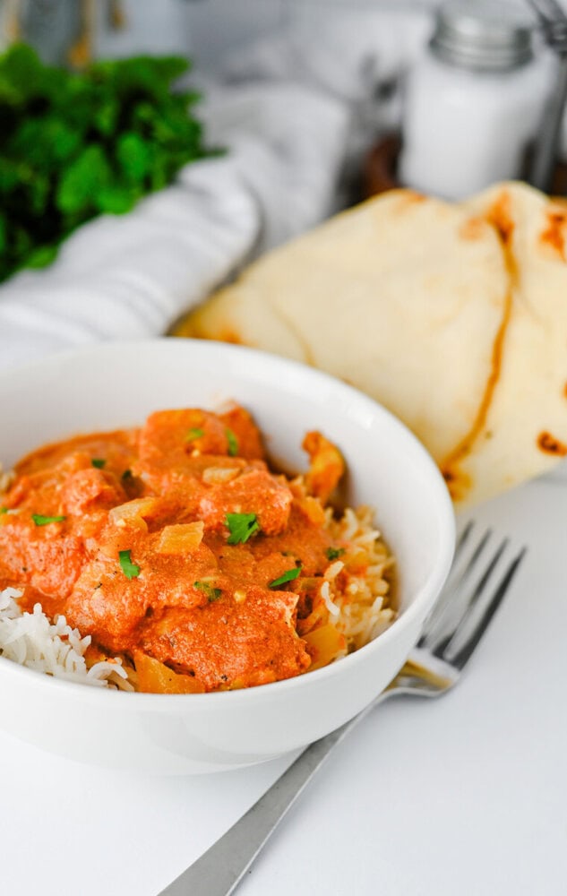 Slow cooker chicken tikka masala served over rice with naan bread and fresh parsley garnish