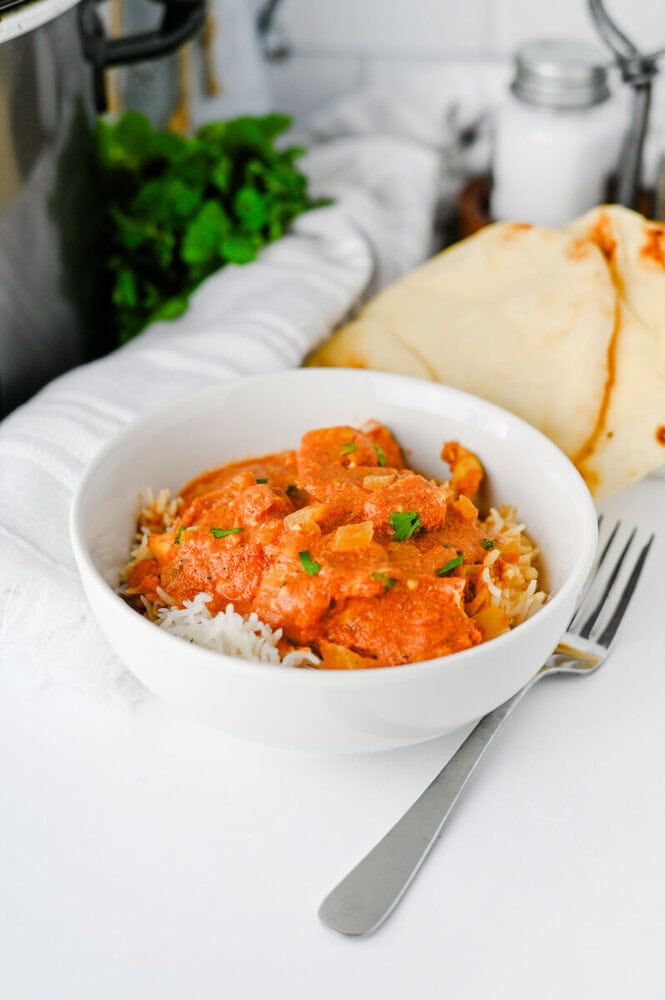 Slow cooker chicken tikka masala served over rice in white bowl with naan bread and fresh cilantro garnish
