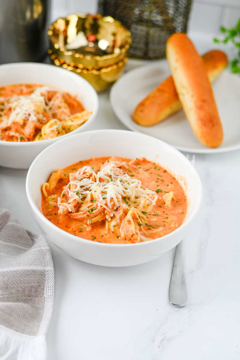 Crock Pot Chicken Tortellini in creamy red sauce with melted cheese garnish served in white bowl
