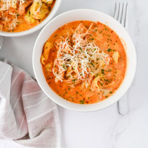 Crock Pot Chicken Tortellini in creamy tomato sauce topped with melted cheese and fresh parsley, plated in white bowls
