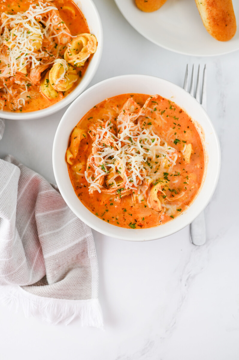 Crock Pot Chicken Tortellini in creamy tomato sauce topped with melted cheese and fresh parsley, plated in white bowls