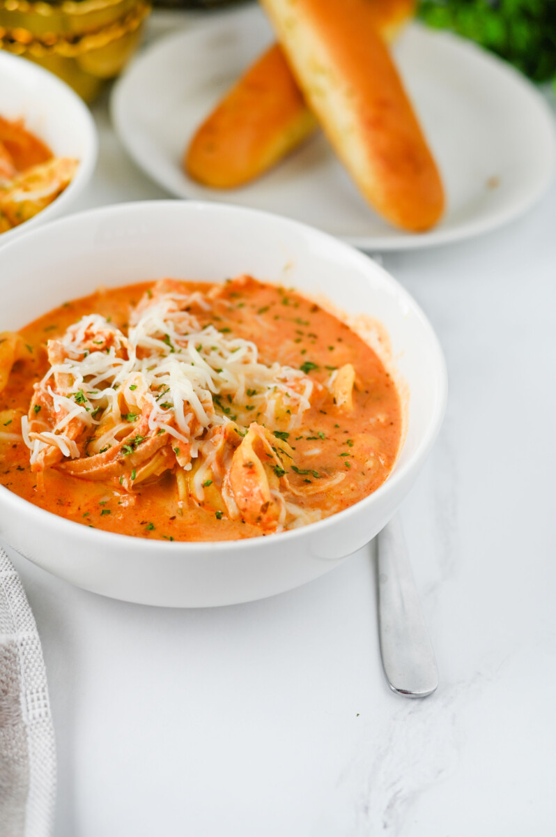 Bowl of creamy Crock Pot Chicken Tortellini with melted cheese garnish and fresh parsley, served with crusty bread