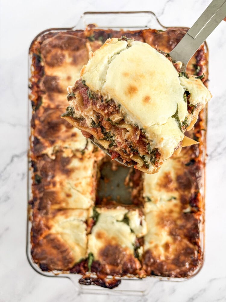Baked 5-cheese lasagna with melted cheese on top, slice being served on spatula from rectangular baking dish