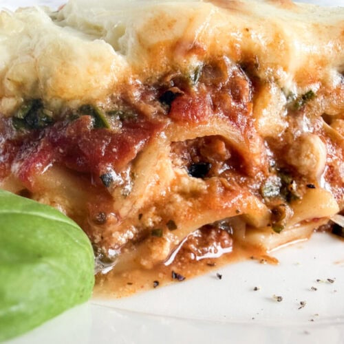 Slice of five cheese lasagna with melted cheese top and meat sauce, garnished with fresh basil