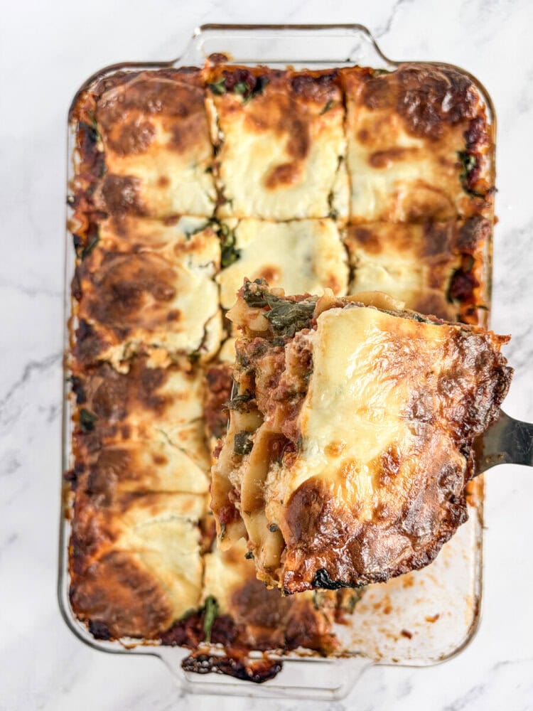 Baked 5-cheese lasagna in glass dish with slice being served, golden brown top with melted cheese