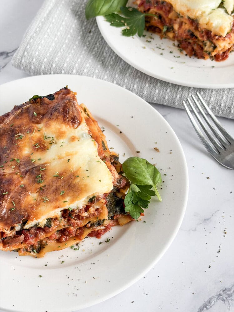 Baked 5-cheese lasagna slice plated with melted cheese topping and fresh basil garnish