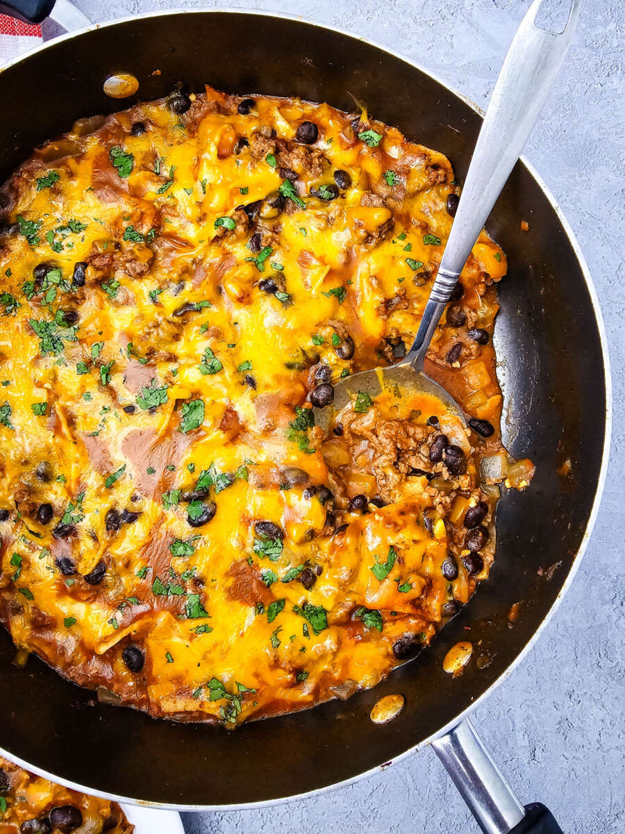 Beef enchiladas skillet with melted cheddar cheese, black beans, and fresh cilantro garnish in cast iron pan