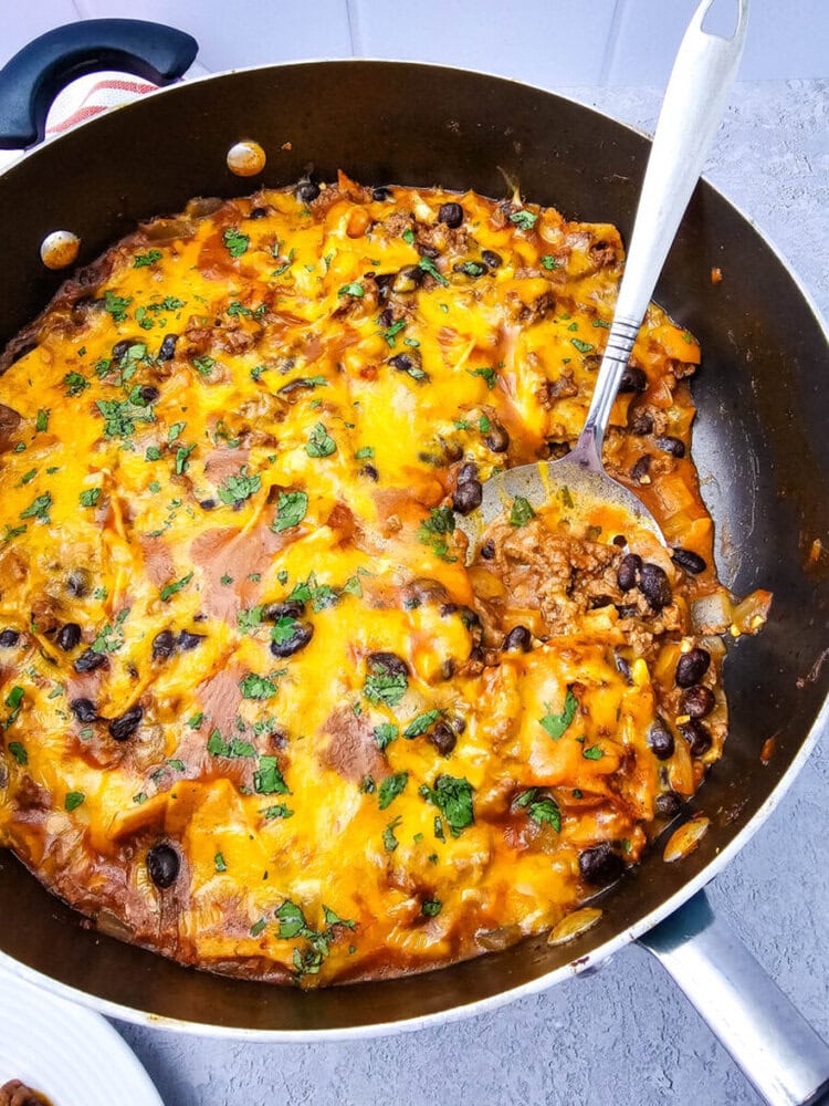 Beef enchiladas skillet with melted cheddar cheese, black beans, and cilantro garnish in a cast iron pan