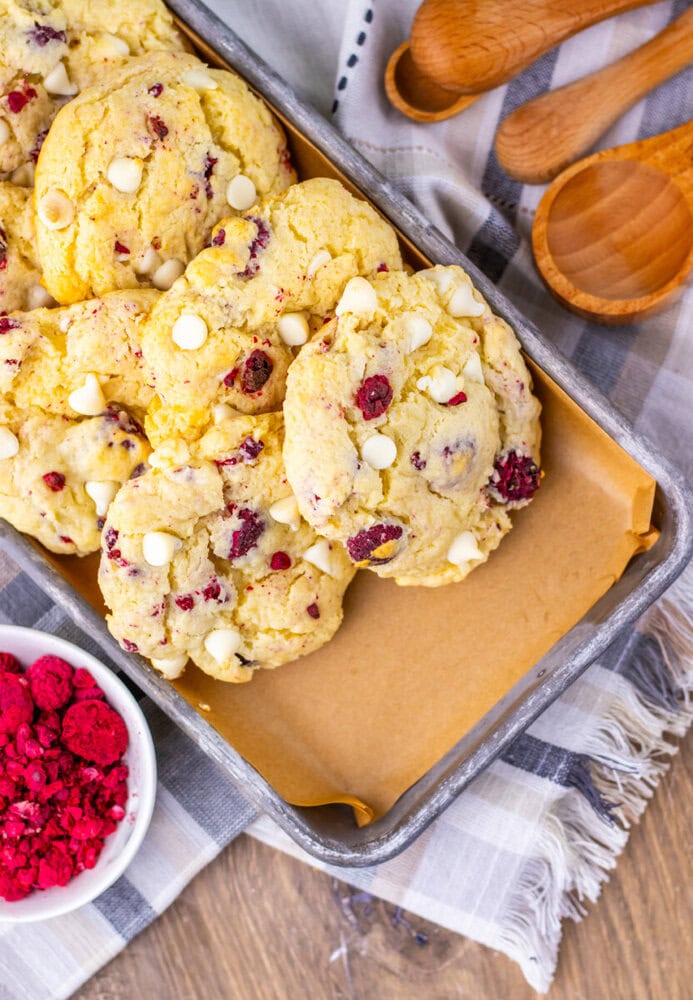 Raspberry cheesecake cookies with white chocolate chips on baking tray with fresh raspberries