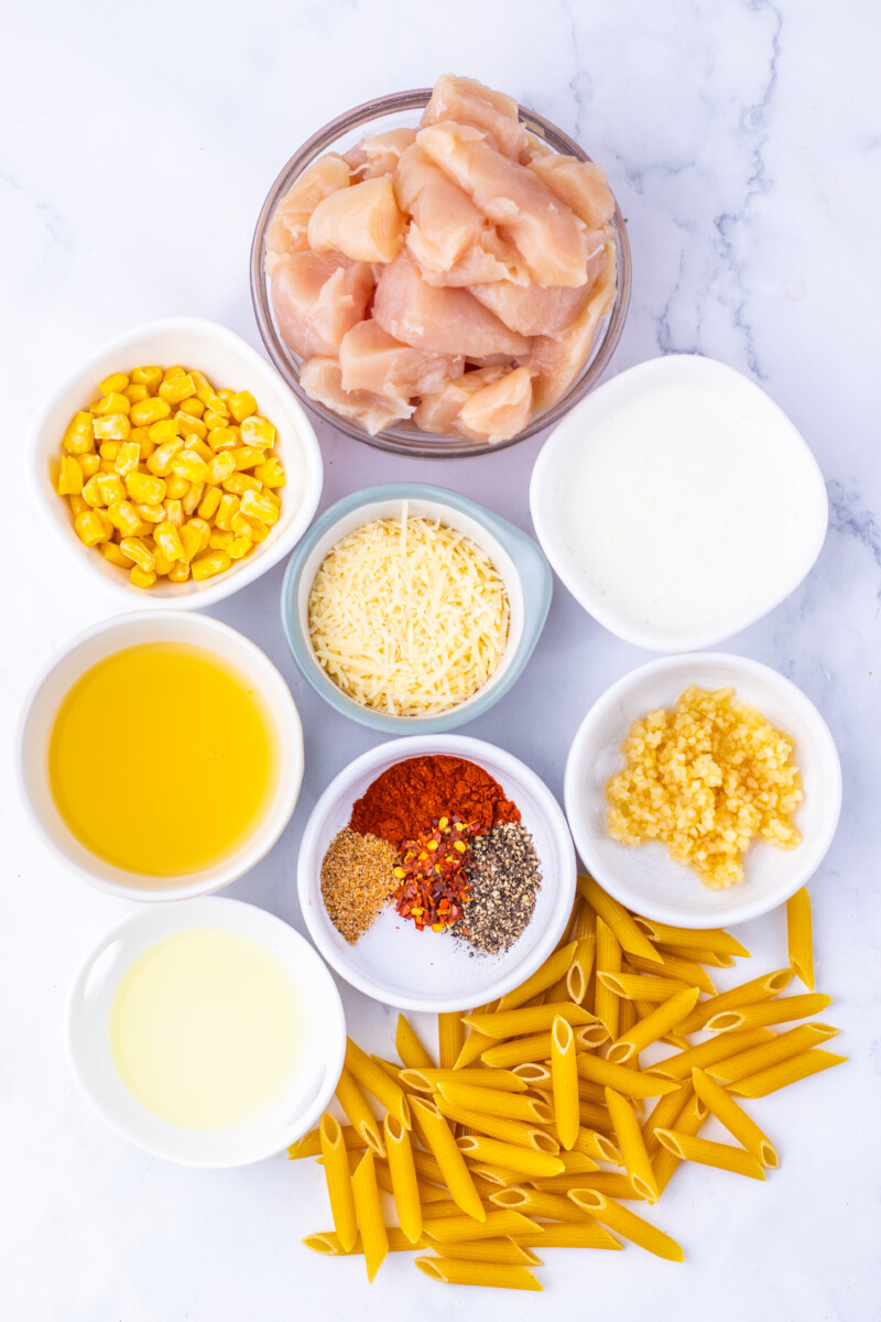 Creamy Cajun Corn Chicken Pasta ingredients laid out in bowls before cooking - chicken, corn, cheese, pasta, oil, cream, and spices