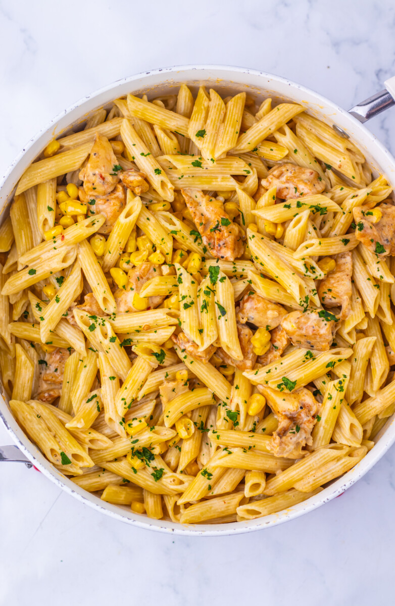 Creamy Cajun corn chicken pasta in white skillet, top view, garnished with parsley