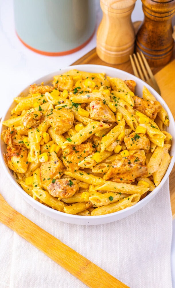 Creamy Cajun corn chicken pasta with herbs in white bowl, ready to serve