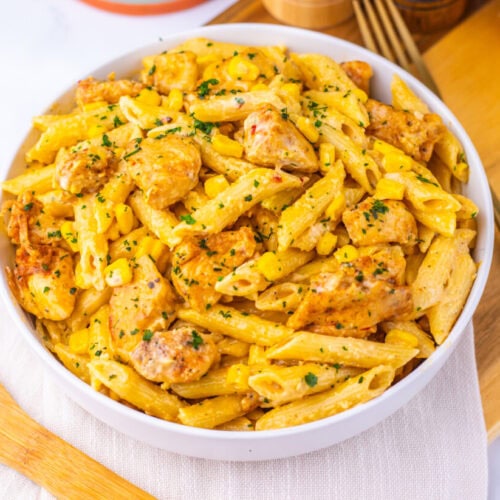 Creamy Cajun Corn Chicken Pasta in white bowl garnished with parsley, served on wooden board