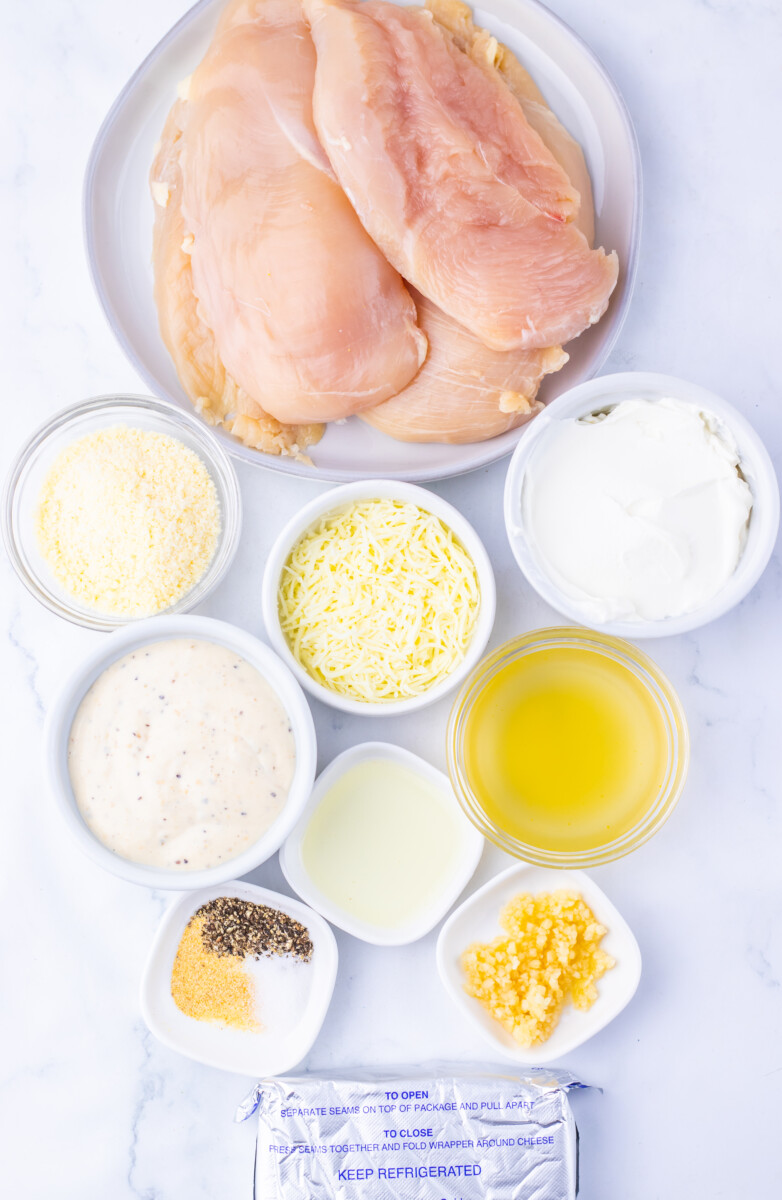 Creamy Caesar chicken bake ingredients laid out - raw chicken breasts, grated Parmesan, shredded mozzarella, mayo, sour cream, olive oil, garlic, and corn kernels