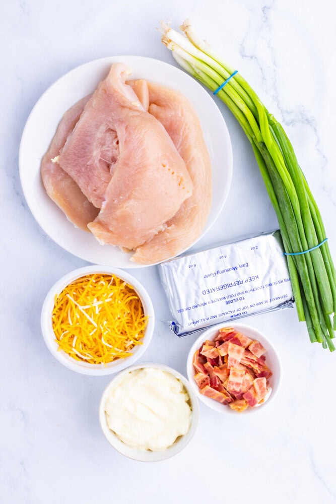 Million Dollar Baked Chicken ingredients laid out including raw chicken breasts, cheddar cheese, cream cheese, bacon, and green onions
