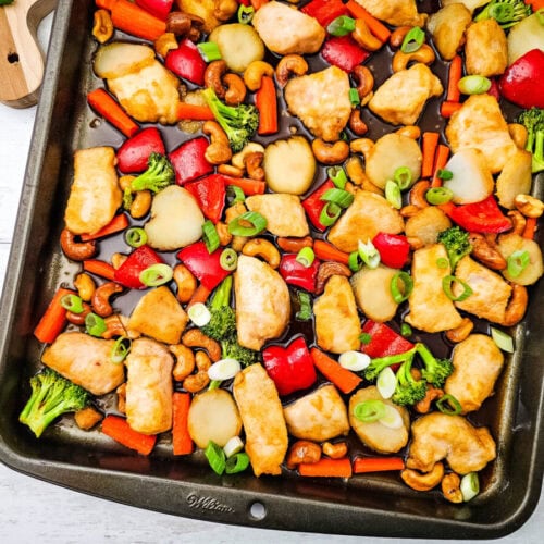 Sheet pan cashew chicken with roasted broccoli, red peppers, and mushrooms garnished with green onions