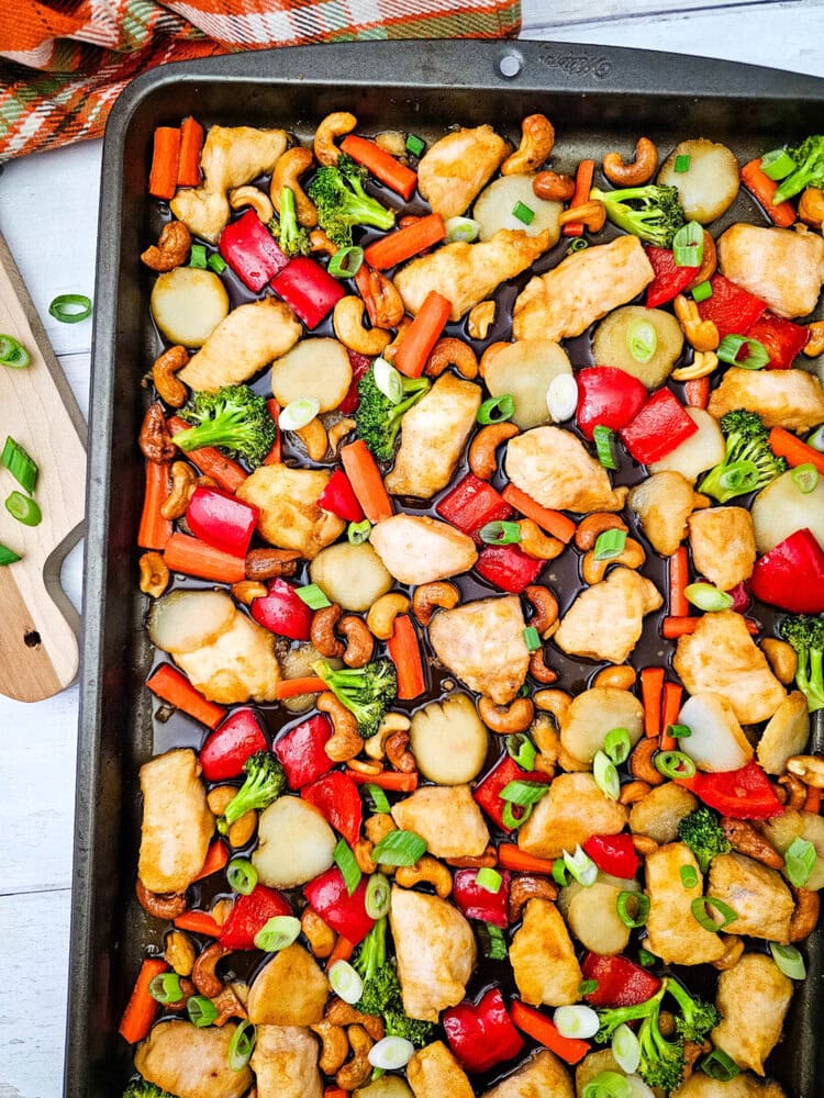 Sheet pan cashew chicken with broccoli, peppers, and cashews garnished with green onions