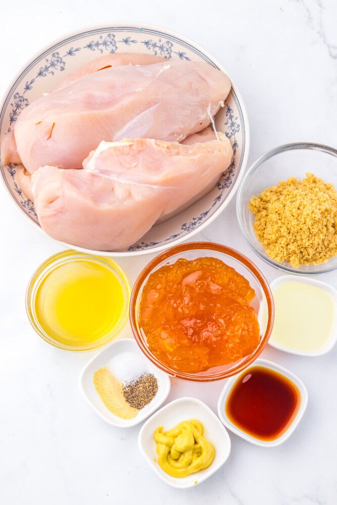Slow cooker apricot brown sugar chicken ingredients laid out including raw chicken breasts, apricot preserves, brown sugar, oil, and spices