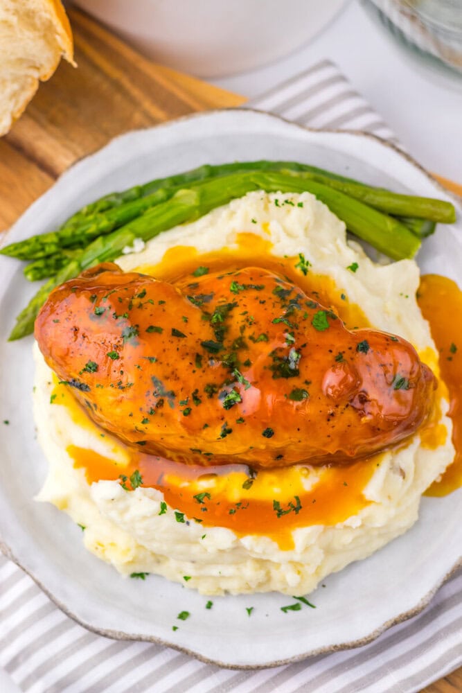 Slow cooker apricot brown sugar chicken served with mashed potatoes and asparagus on a white plate