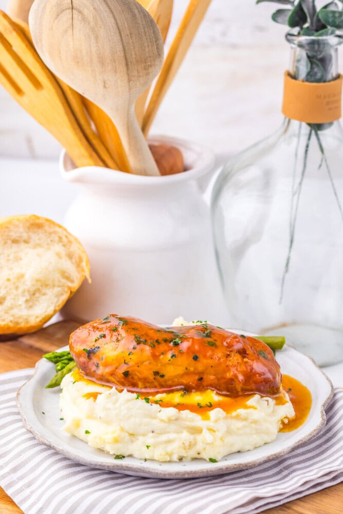 Slow cooker apricot brown sugar chicken served over mashed potatoes with asparagus and fresh herbs