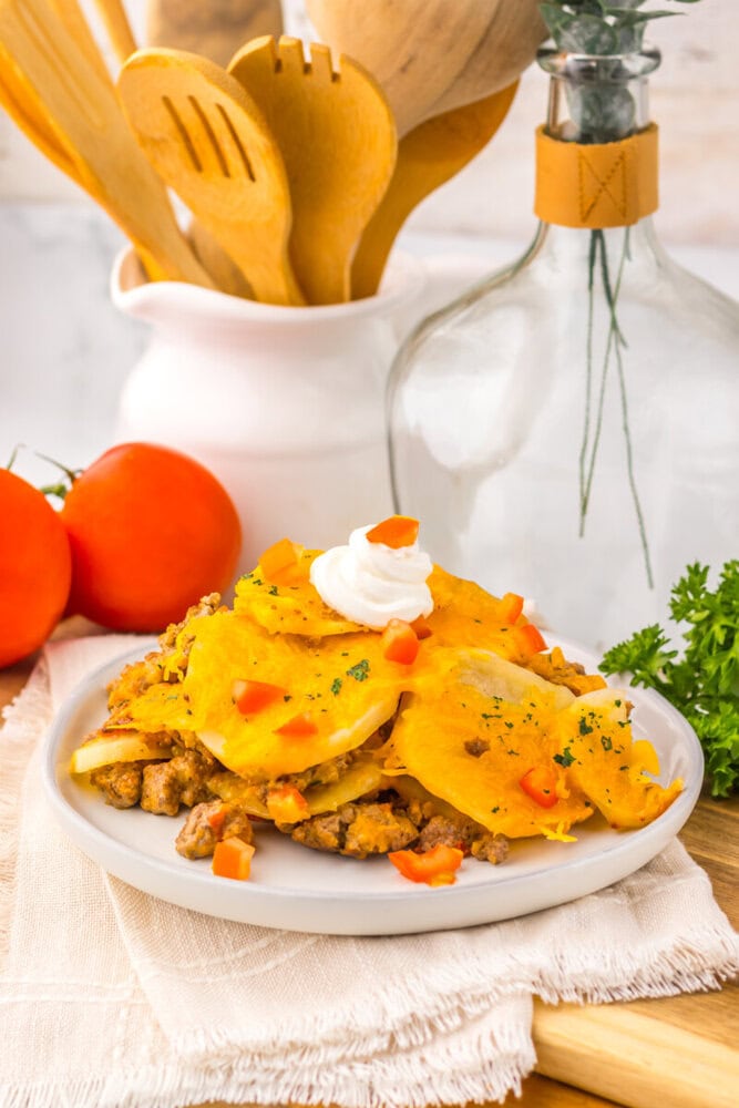 Slow cooker cheesy taco potato casserole with ground meat, melted cheese, diced peppers, and sour cream on white plate