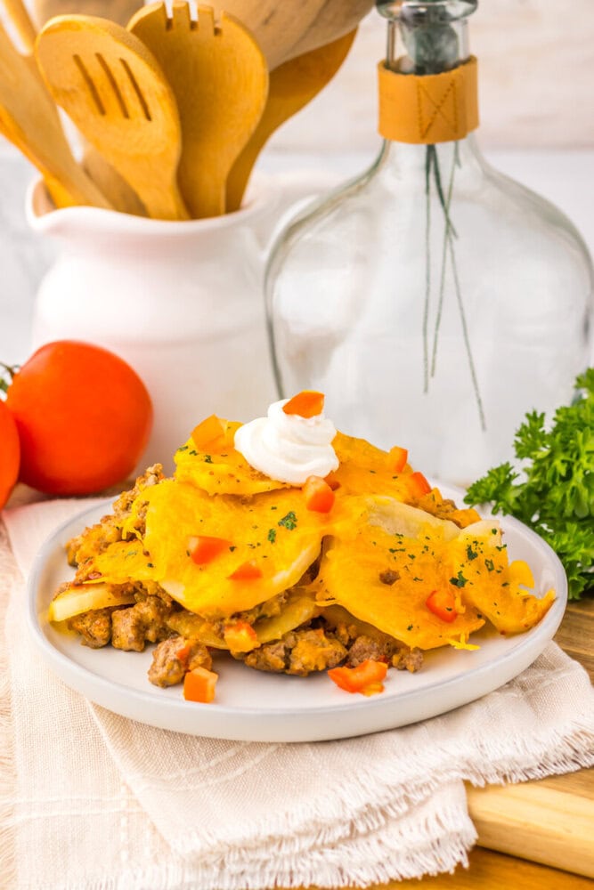 Slow cooker cheesy taco potato casserole plated with sour cream topping and diced vegetables