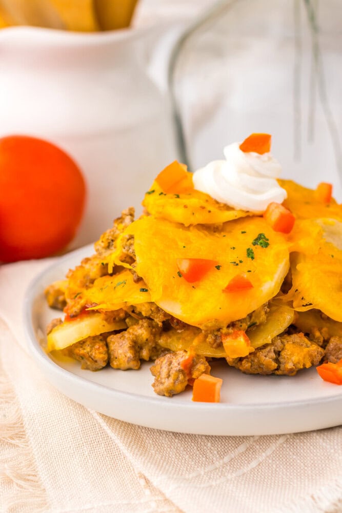 Slow cooker cheesy taco potato casserole with ground meat, topped with melted cheese, sour cream, and fresh diced tomatoes