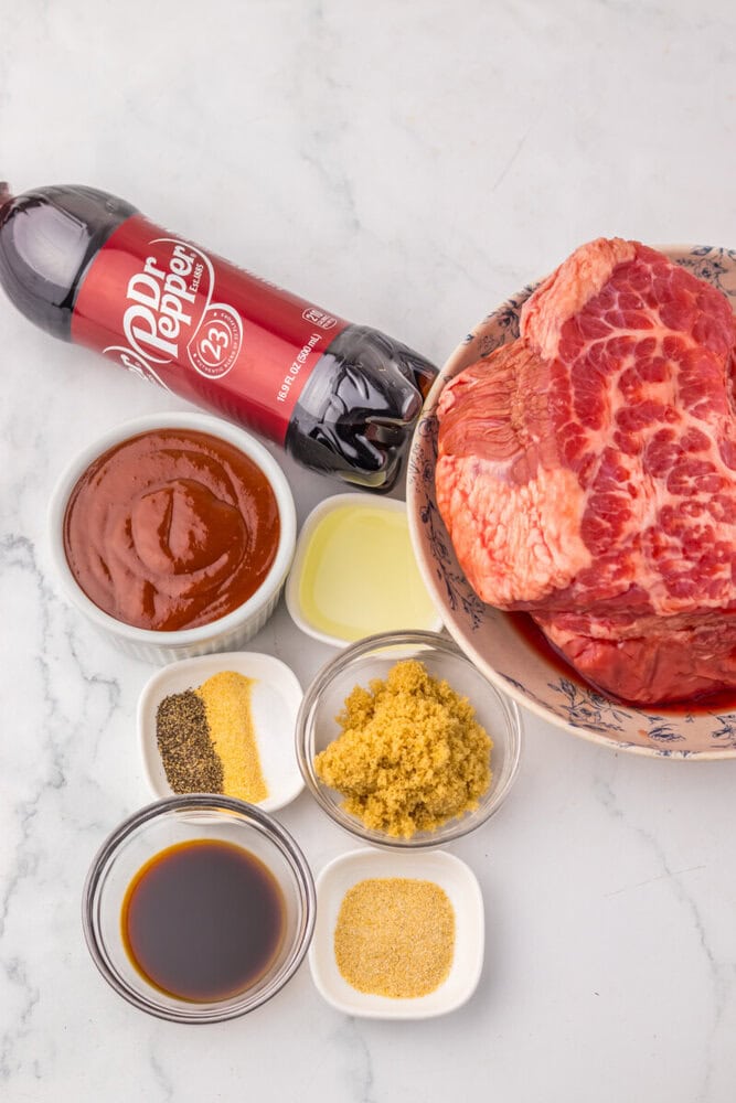 Slow Cooker Dr Pepper BBQ Brisket ingredients laid out including raw brisket, Dr Pepper, BBQ sauce, and spices