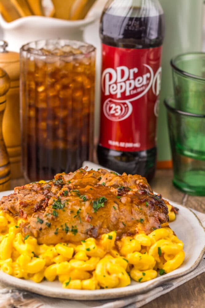 Slow cooker Dr Pepper BBQ brisket with corn on white plate, Dr Pepper bottle and drinks in background