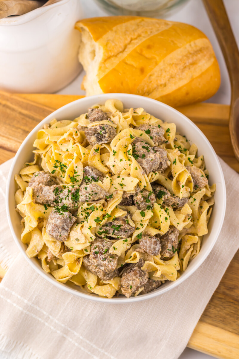 Slow cooker garlic butter beef and noodles in white bowl with fresh parsley garnish and bread