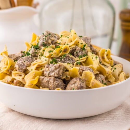 Slow cooker garlic butter beef and noodles in white bowl with parsley garnish