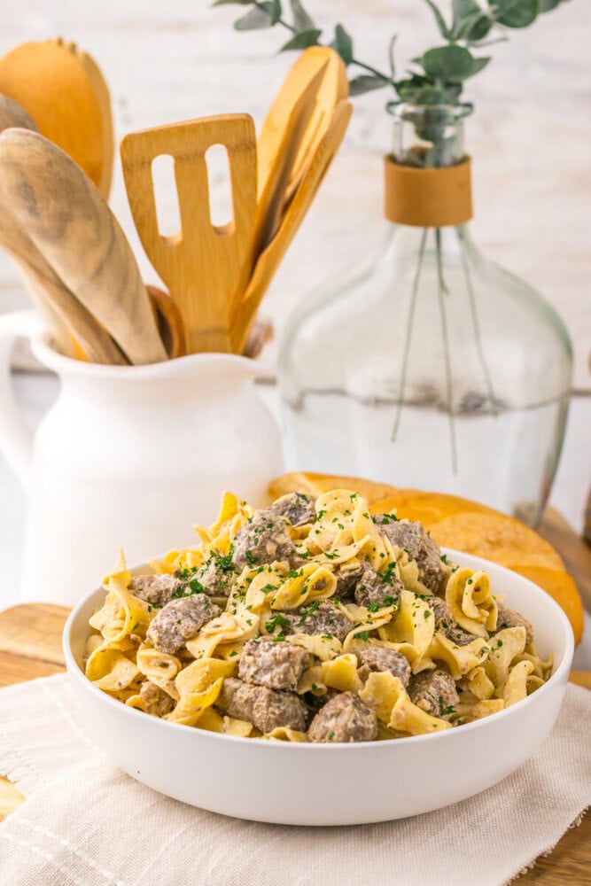 Slow cooker garlic butter beef and noodles in white bowl with herb garnish and wooden spoon