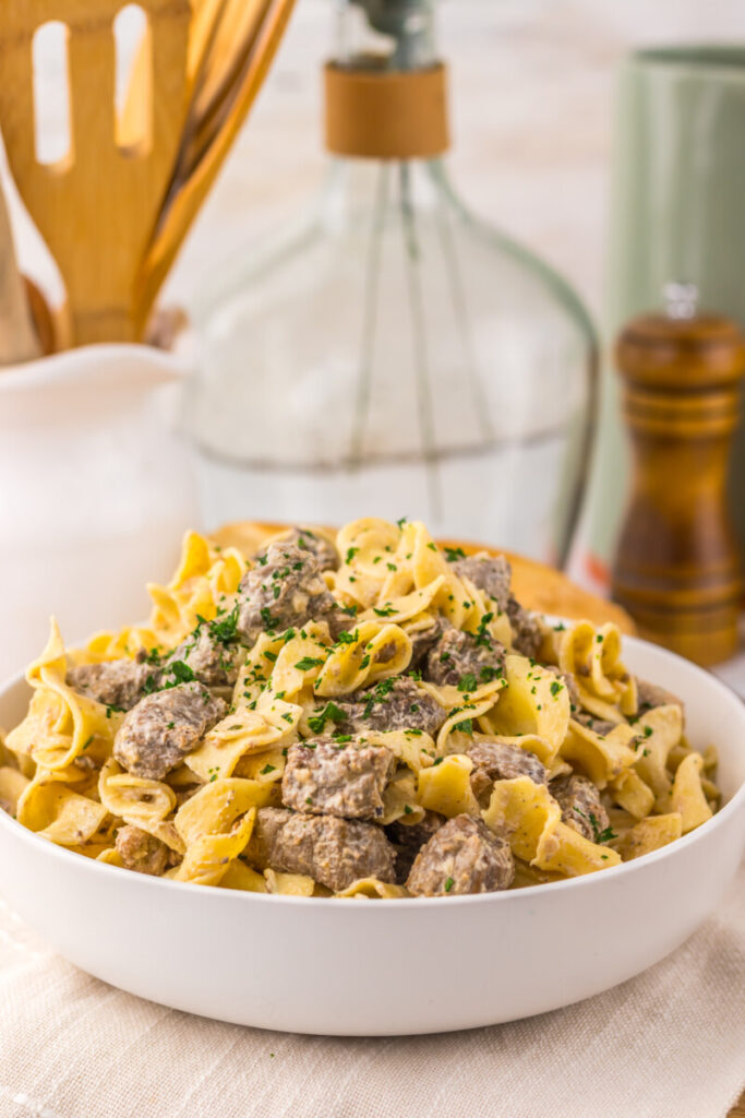Slow cooker garlic butter beef and noodles plated in white bowl with fresh parsley garnish
