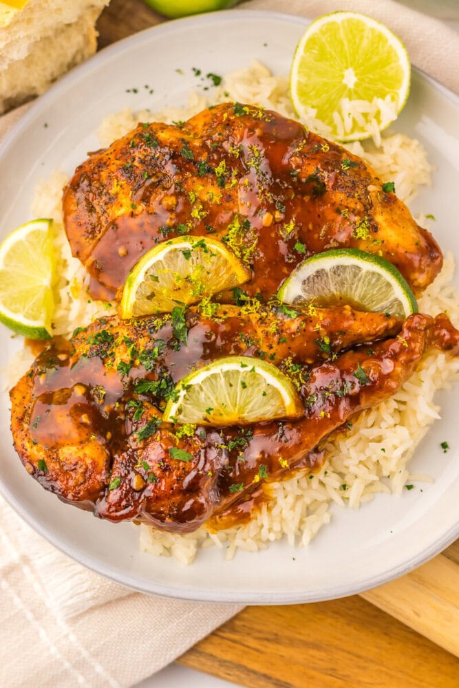 Slow cooker honey lime chicken with caramelized glaze, lime garnish, and rice on white plate