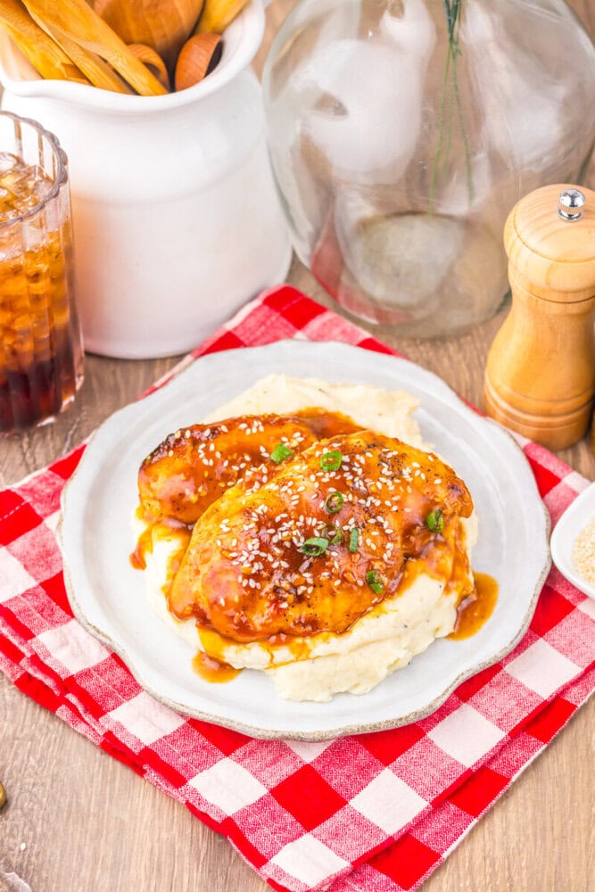 Slow cooker honey sesame chicken served over mashed potatoes with sesame seed garnish on white plate
