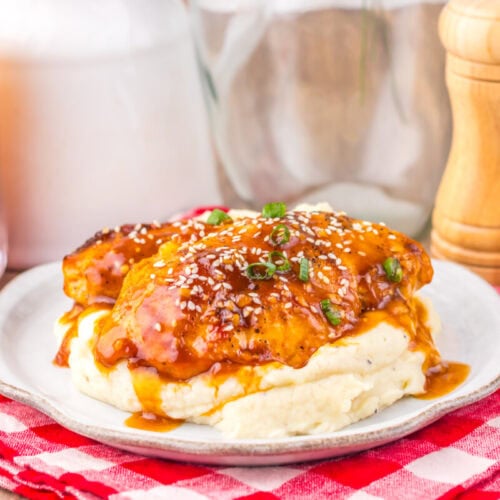 Slow cooker honey sesame chicken with sesame seeds and green onions served over mashed potatoes on white plate