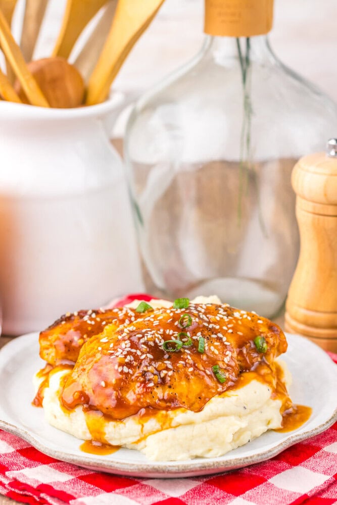 Slow cooker honey sesame chicken with sesame seeds and scallions served over mashed potatoes