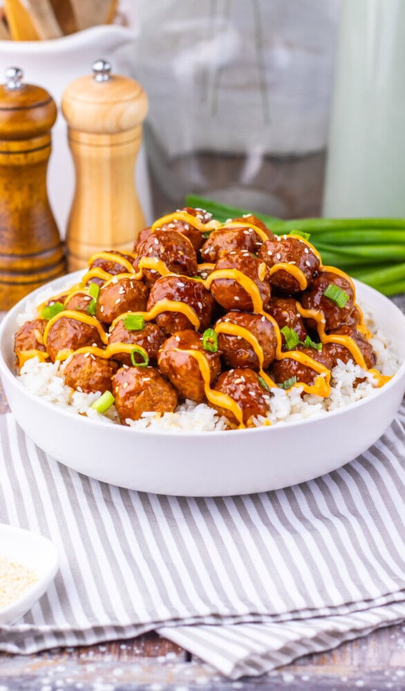 Slow cooker Korean BBQ meatballs over rice with peppers and green onions in white bowl