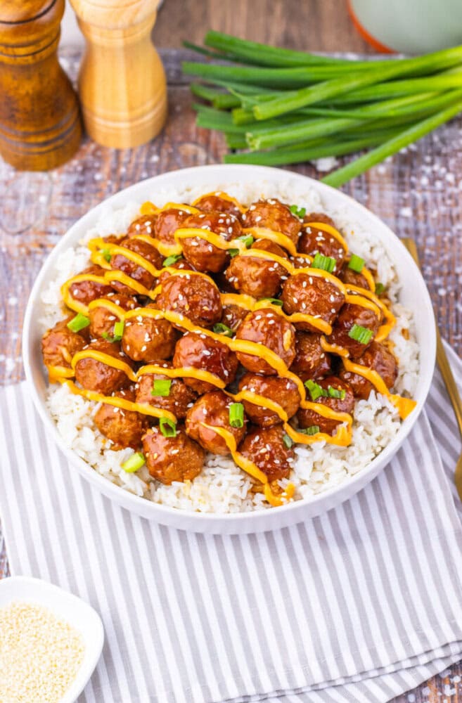 Slow cooker Korean BBQ meatballs with sesame seeds and green onions served over rice on a white plate