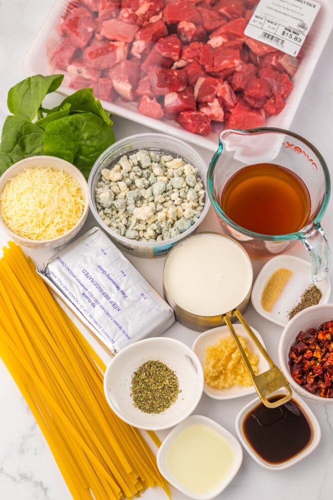 Slow Cooker Copycat Olive Garden Steak Gorgonzola ingredients laid out including raw beef, pasta, gorgonzola cheese, cream, broth, and seasonings