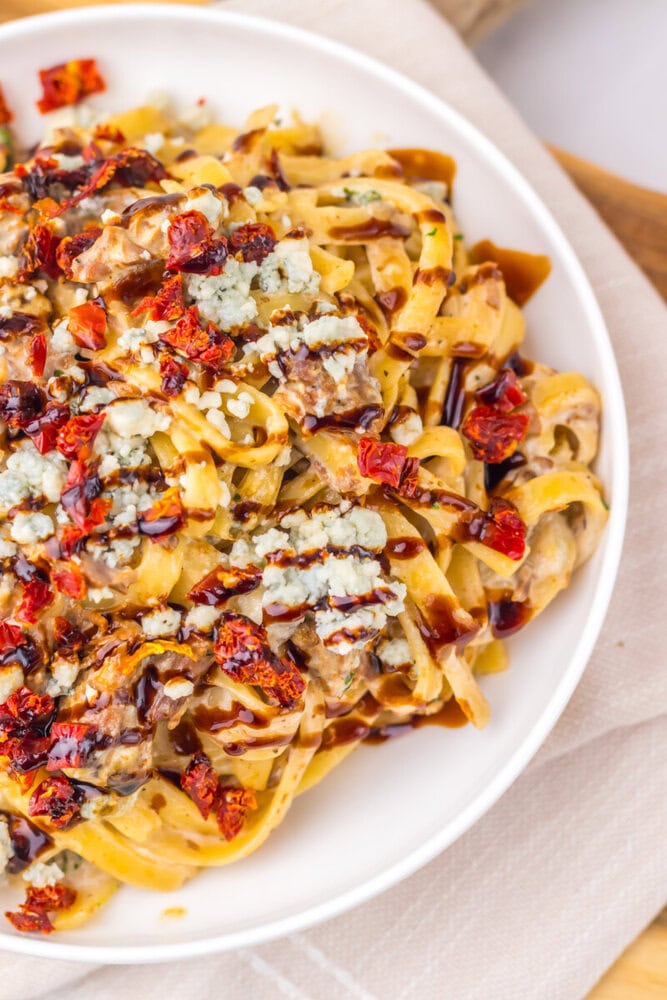 Slow Cooker Steak Gorgonzola pasta with ribbon noodles, melted blue cheese, bacon, and sun-dried tomatoes on white plate