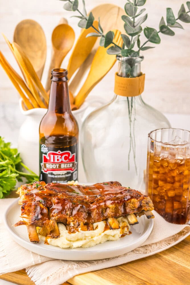 Slow cooker root beer BBQ ribs served on mashed potatoes with root beer bottle and glass