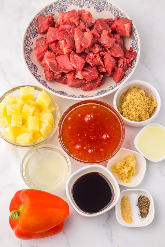 Ingredients for slow cooker sweet chili pineapple steak tips including diced beef, pineapple chunks, red bell pepper, and seasonings arranged in bowls