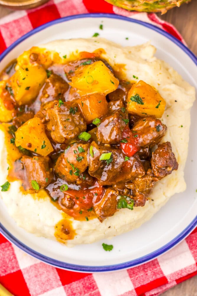 Slow cooker sweet chili pineapple steak tips with pineapple chunks served over mashed potatoes, garnished with fresh parsley